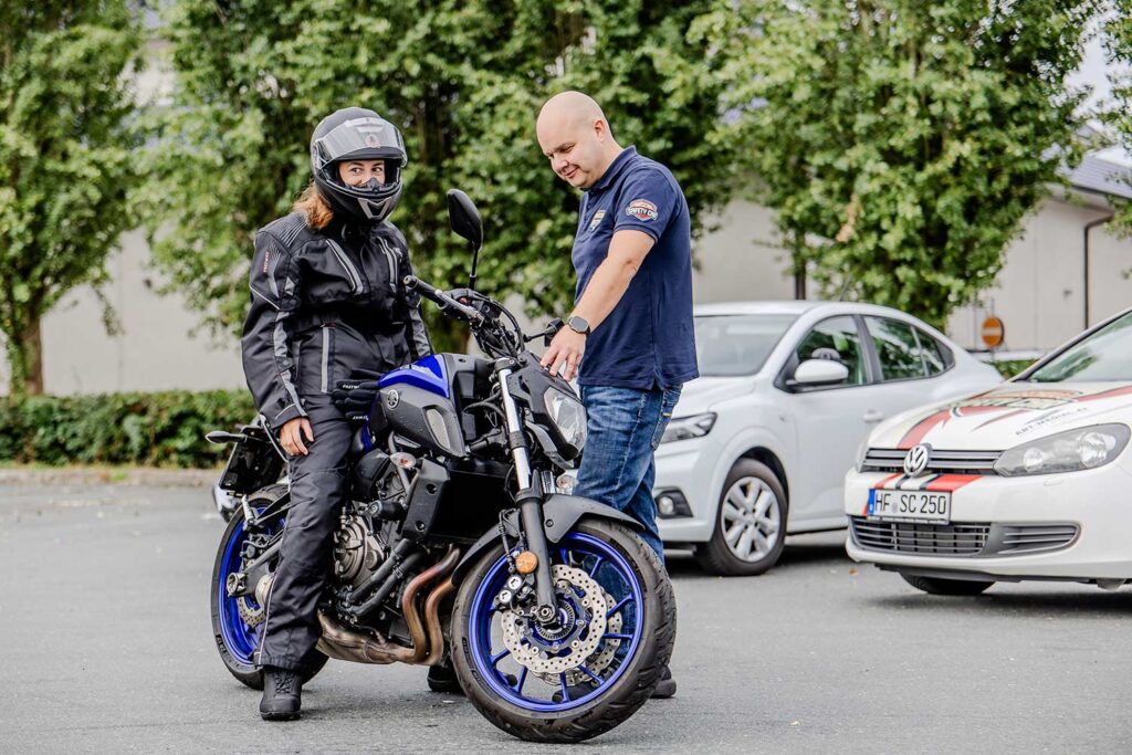 Ein Fahrlehrer erklärt einer Fahrschülerin die auf einem Motorrad sitzt etwas zu den Motorrad-Anzeigen.