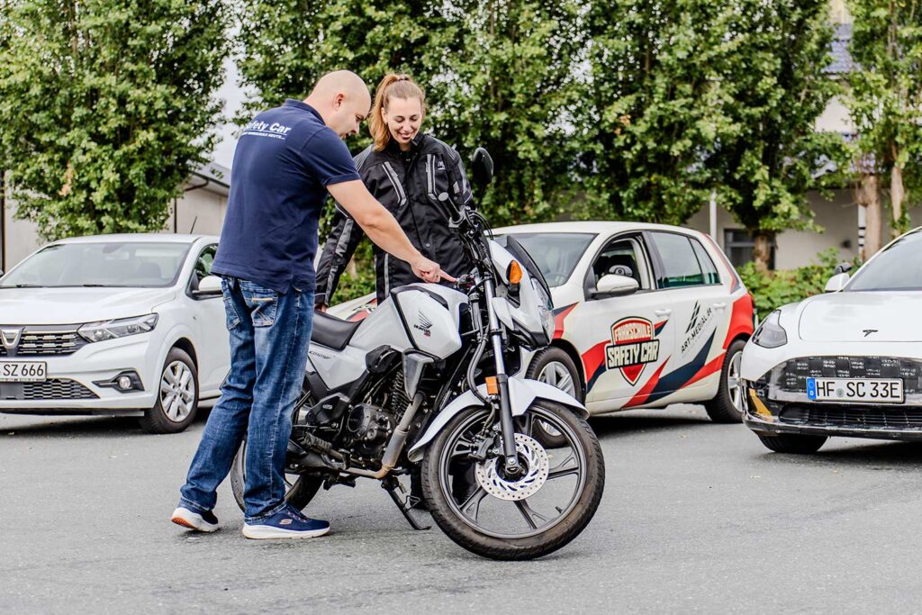 Ein Fahrlehrer erklärt einer Fahrschülerin die neben einem Motorrad steht etwas zu dem Motorrad.
