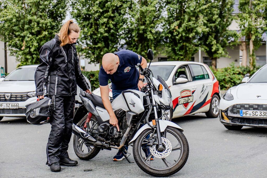 Ein Fahrlehrer zeigt seiner Fahrschülerin worauf sie beim Motorrad achten muss.