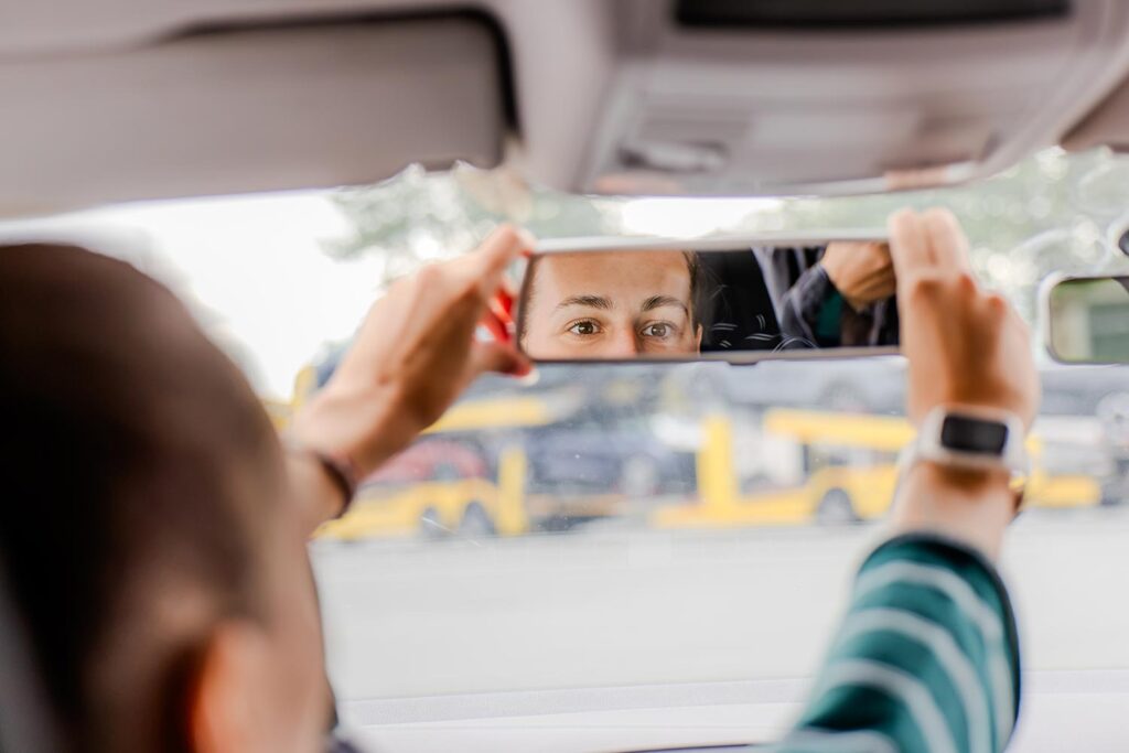 Eine Fahrschülerin ist in einer Fahrstunde und richtet grade den Rückspiegel der Autor aus.