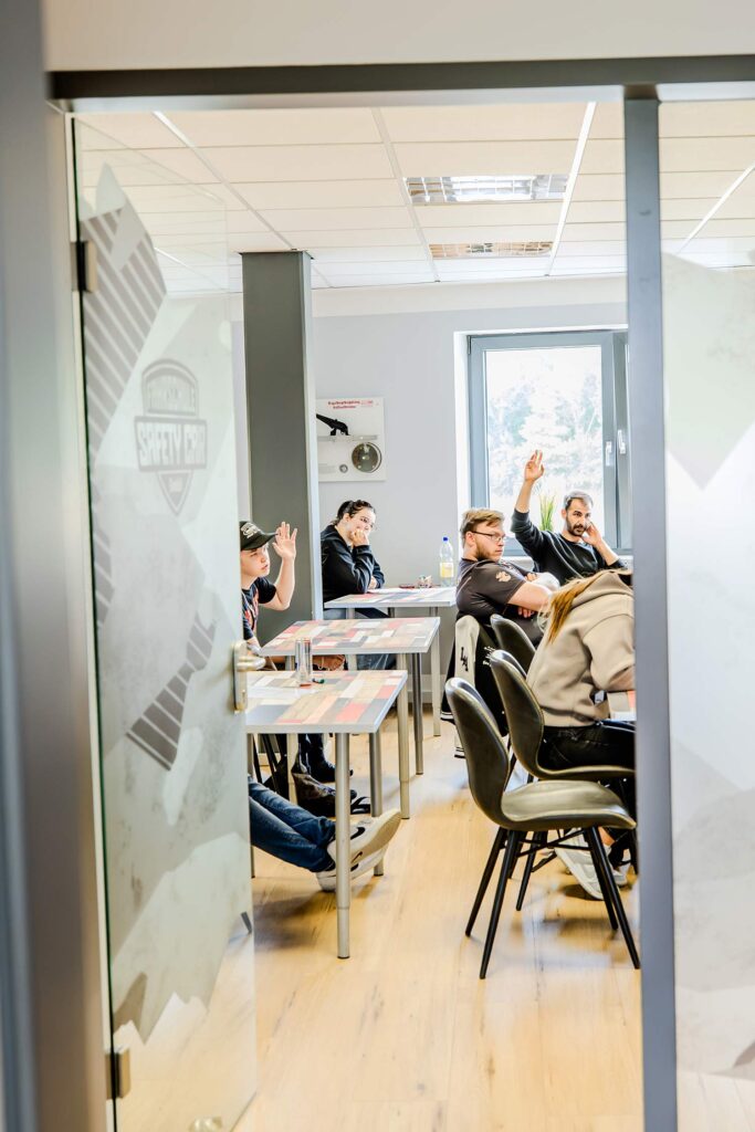 Eine offene Tür durch, welche man in einem Seminarraum schauen kann in, welchem gerade eine Theoriespunde statt findet.