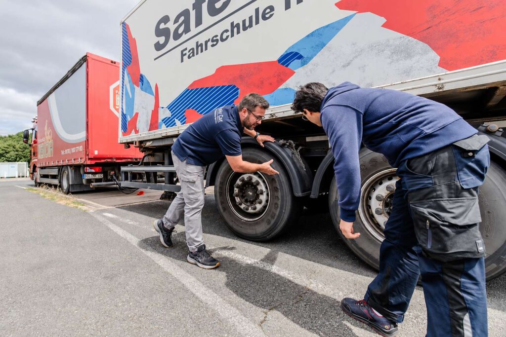 Fahrlehrer erklärt dem Fahrschüler die Reifen und den Reifendruck bei dem LKW Anhänger.
