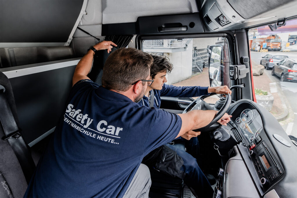 Fahrlehrer und Fahrschüler bei einer LKW Fahrstunde. Fahrlehrer erklärt dem Schüler die Anzeigen im Cockpit.