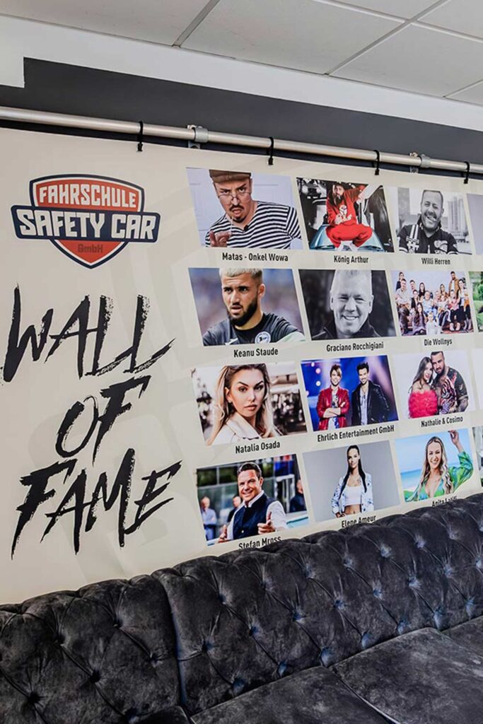 Ein Plakat im Eingangsbereich der Fahrschule auf welchem "Wall of Fame" steht und viele Prominente und bekannte Persönlichkeiten zu sehen sind die an der Fahrschule eine Fahrausbildung gemacht haben.