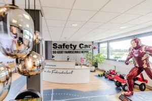 Eingangsbereich der Fahrschule Safety Car mit Ironman Statue, Rezeption, Rutschautos, Straßensticker auf dem Flurboden und Pflanzen.