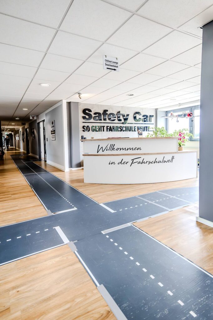 Der Eingangsbereich der Safety Car Fahrschule mit dem Eingangstresen und Straßen-Folierung auf dem Flurboden.